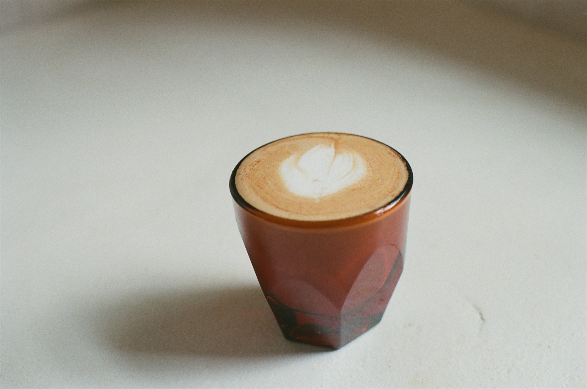 A latte in an amber glass on a pale surface