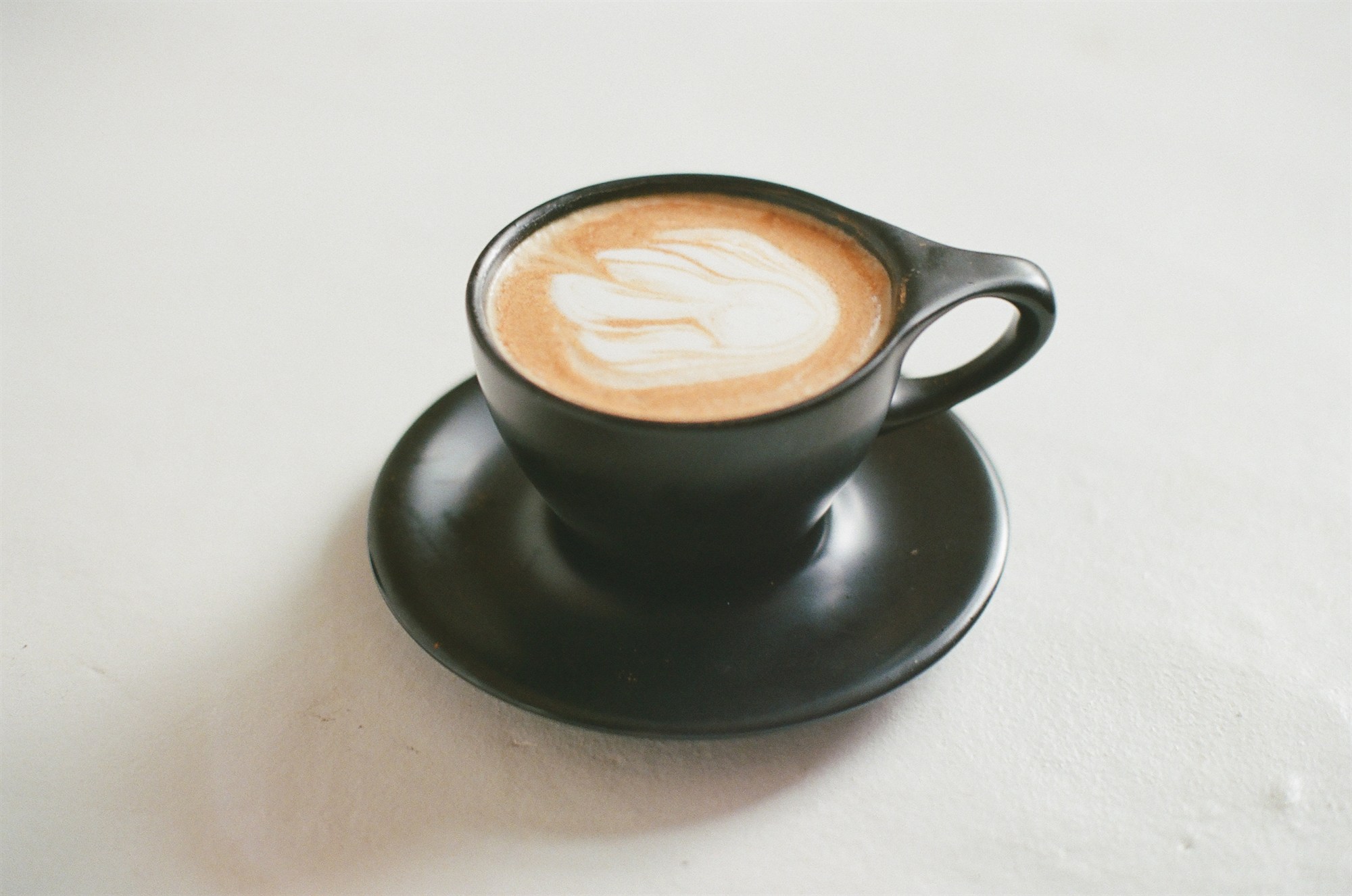 A black cup and saucer with latte art on white